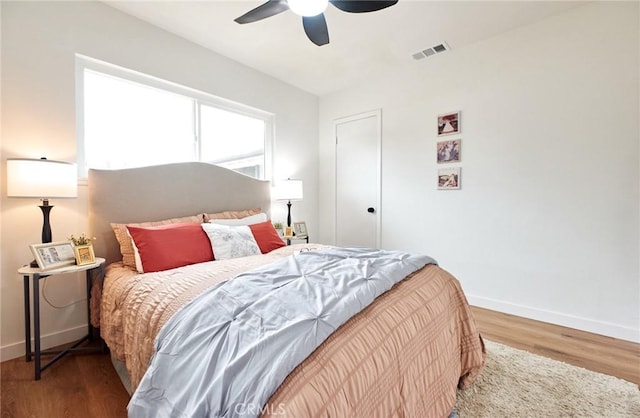 bedroom with ceiling fan, visible vents, baseboards, and wood finished floors