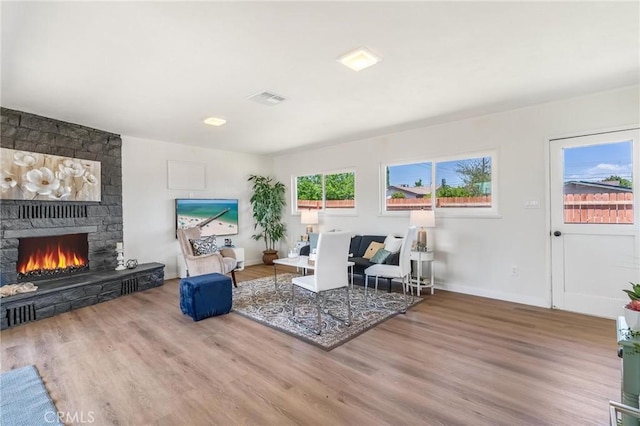 living area featuring a stone fireplace, wood finished floors, and baseboards