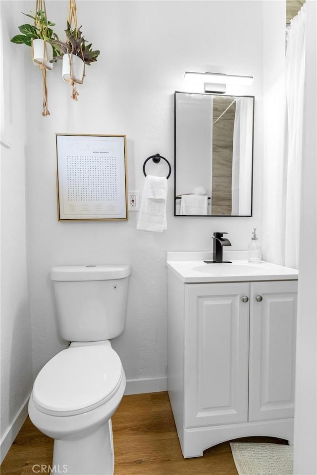 bathroom featuring baseboards, wood finished floors, toilet, and vanity