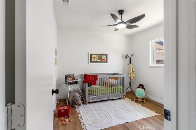 bedroom featuring a nursery area, wood finished floors, baseboards, and ceiling fan