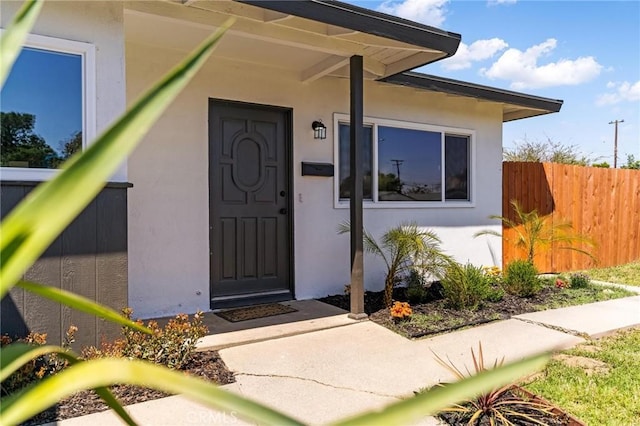 doorway to property with stucco siding and fence