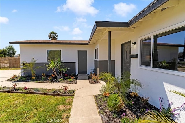 view of exterior entry with stucco siding and fence