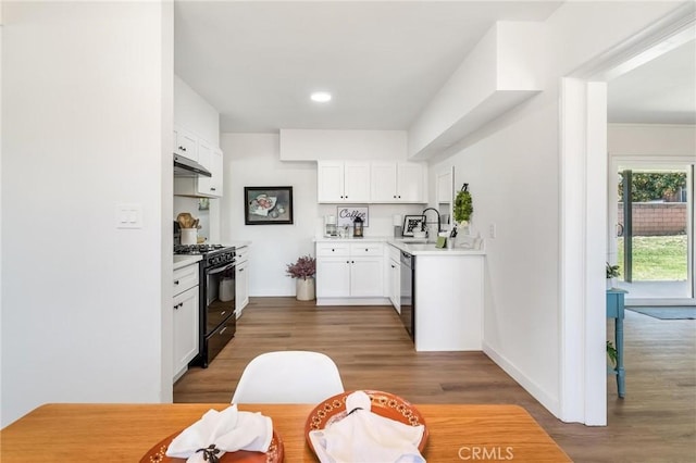 kitchen featuring black gas range oven, under cabinet range hood, stainless steel dishwasher, wood finished floors, and light countertops