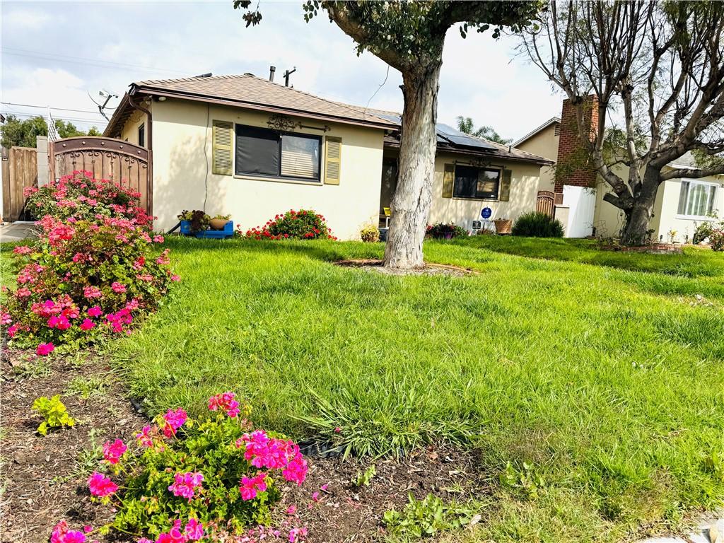 view of front of house with stucco siding, roof mounted solar panels, a front lawn, and fence