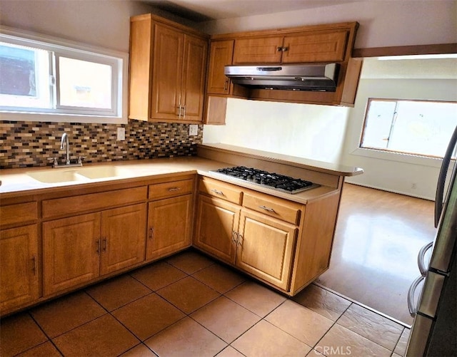 kitchen with under cabinet range hood, tasteful backsplash, light countertops, and a sink