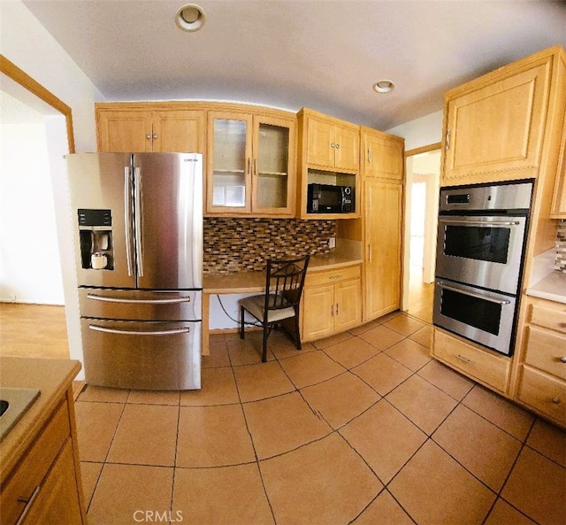 kitchen with tasteful backsplash, appliances with stainless steel finishes, light countertops, light tile patterned floors, and glass insert cabinets