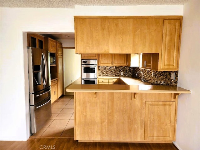 kitchen with backsplash, light countertops, light tile patterned floors, appliances with stainless steel finishes, and a peninsula