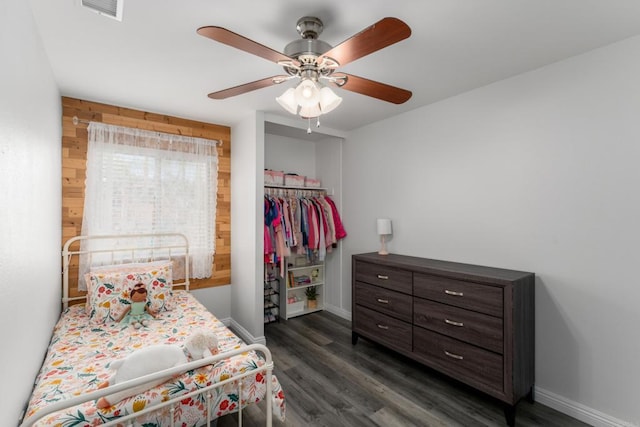 bedroom with dark wood-type flooring, baseboards, wood walls, a closet, and a ceiling fan