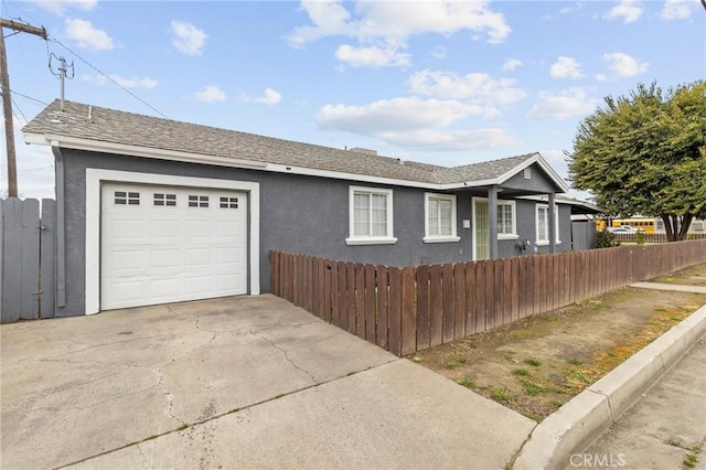 ranch-style home with roof with shingles, an attached garage, stucco siding, concrete driveway, and a fenced front yard