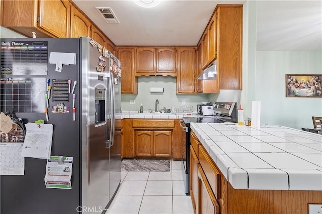 kitchen with light tile patterned floors, visible vents, tile counters, appliances with stainless steel finishes, and under cabinet range hood