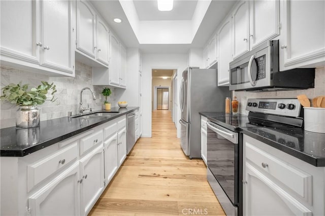 kitchen featuring appliances with stainless steel finishes, white cabinetry, a tray ceiling, and a sink