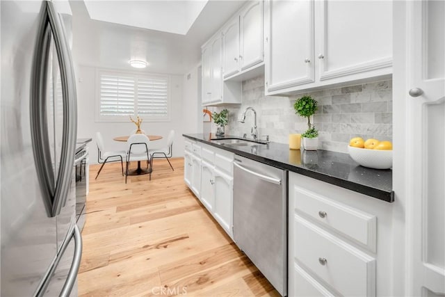 kitchen with light wood-type flooring, a sink, tasteful backsplash, stainless steel appliances, and white cabinets