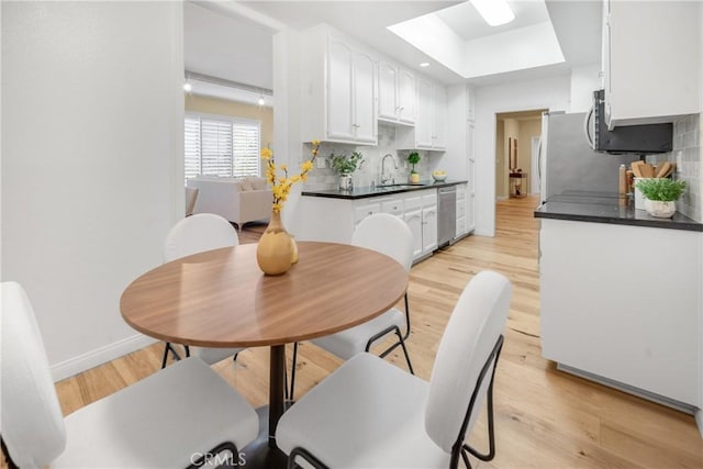 kitchen with light wood-type flooring, dark countertops, white cabinets, a skylight, and a sink