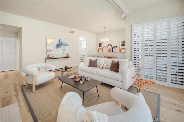 living room featuring visible vents, baseboards, a chandelier, rail lighting, and wood finished floors