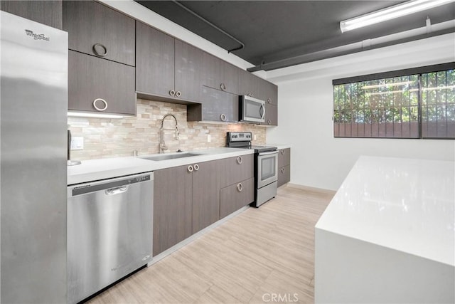 kitchen with light wood-type flooring, light countertops, decorative backsplash, appliances with stainless steel finishes, and a sink