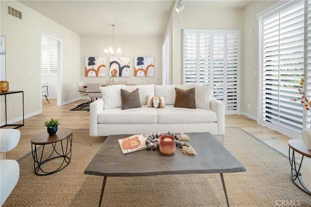 living area with visible vents, baseboards, a chandelier, and wood finished floors