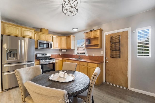 kitchen featuring baseboards, light wood-style flooring, a sink, light brown cabinetry, and stainless steel appliances