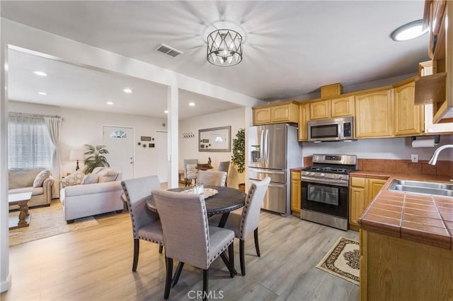 kitchen featuring visible vents, a sink, light wood-style floors, appliances with stainless steel finishes, and tile counters