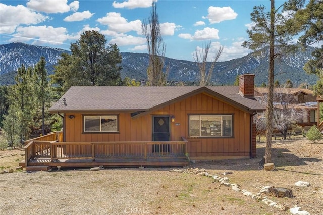 chalet / cabin with a deck with mountain view, a chimney, board and batten siding, and a shingled roof