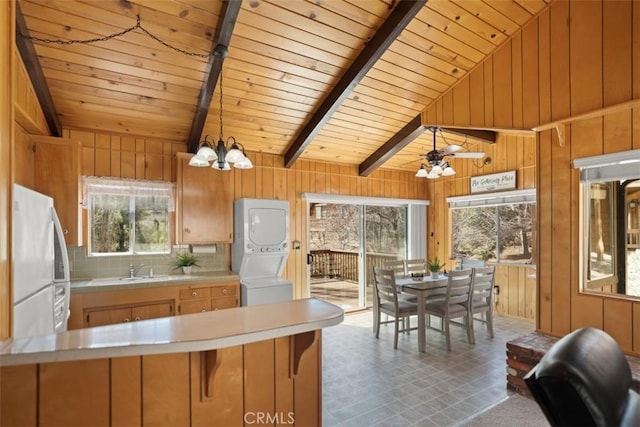 kitchen featuring wooden walls, lofted ceiling with beams, freestanding refrigerator, light countertops, and stacked washer and dryer