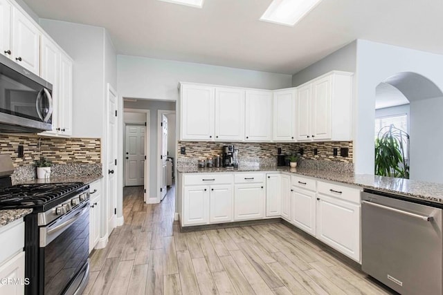 kitchen featuring white cabinets, appliances with stainless steel finishes, light wood-type flooring, and light stone countertops