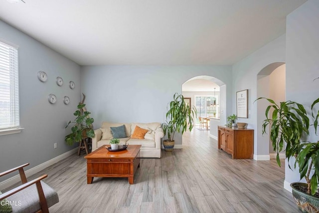 living room with baseboards, arched walkways, and light wood-style flooring