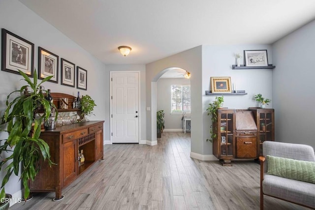 entrance foyer with baseboards, arched walkways, and light wood-style flooring