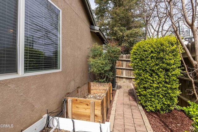 view of side of property with stucco siding, a vegetable garden, and fence