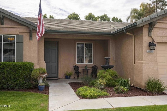 doorway to property with stucco siding, a garage, and a tile roof