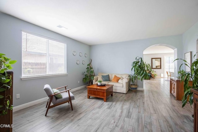 living room featuring arched walkways, visible vents, baseboards, and light wood-style floors