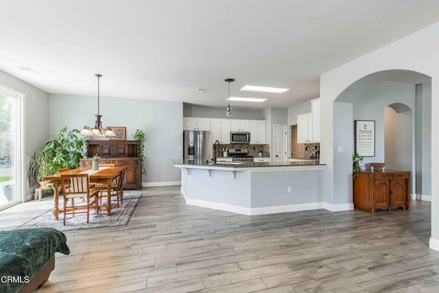 kitchen with a peninsula, light wood-style floors, appliances with stainless steel finishes, white cabinetry, and backsplash