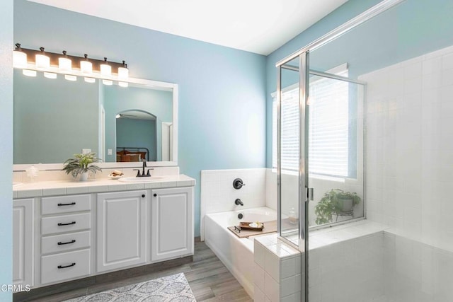 bathroom featuring a stall shower, a sink, wood finished floors, double vanity, and a bath