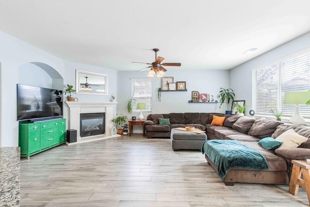 living area with a glass covered fireplace, visible vents, light wood finished floors, and ceiling fan