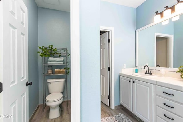 bathroom featuring toilet, vanity, baseboards, and wood finished floors