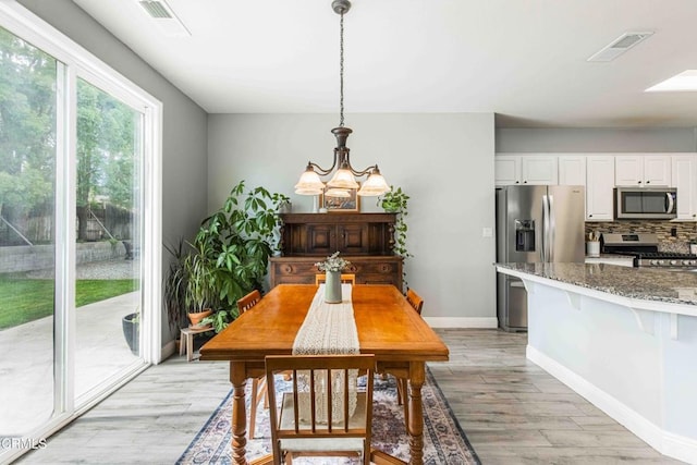 dining room with light wood-style flooring, a notable chandelier, baseboards, and visible vents