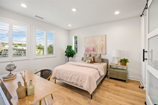 bedroom with recessed lighting, visible vents, a barn door, and light wood-style floors