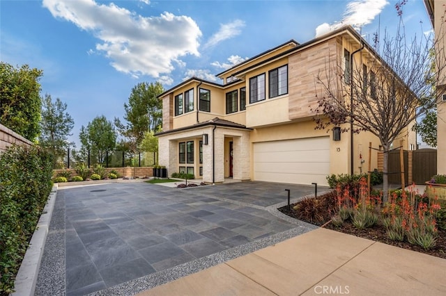 view of front facade with an attached garage, fence, driveway, and stucco siding