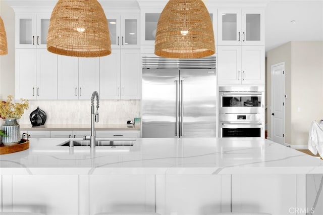 kitchen featuring a sink, light stone counters, tasteful backsplash, stainless steel appliances, and white cabinets