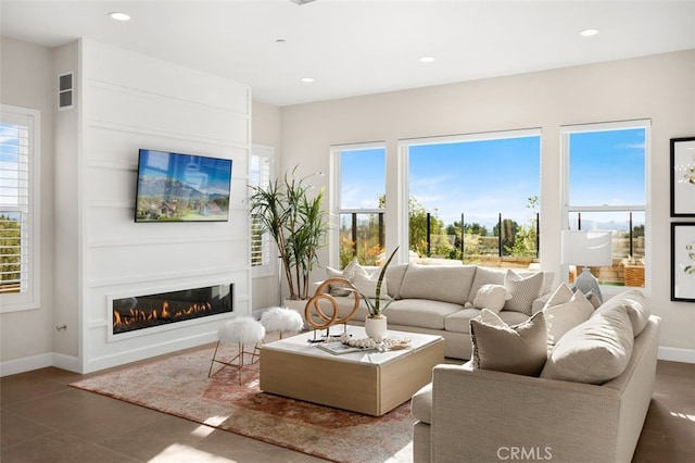 living room featuring recessed lighting, baseboards, plenty of natural light, and a glass covered fireplace