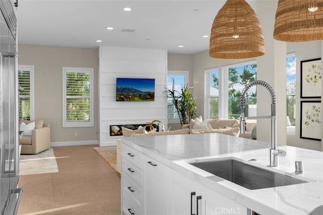 kitchen featuring open floor plan, light stone countertops, white cabinetry, and a sink