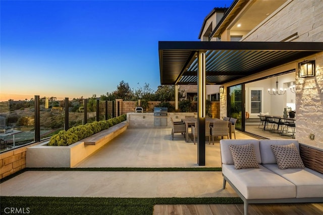 patio terrace at dusk with grilling area, outdoor dining area, exterior kitchen, and fence