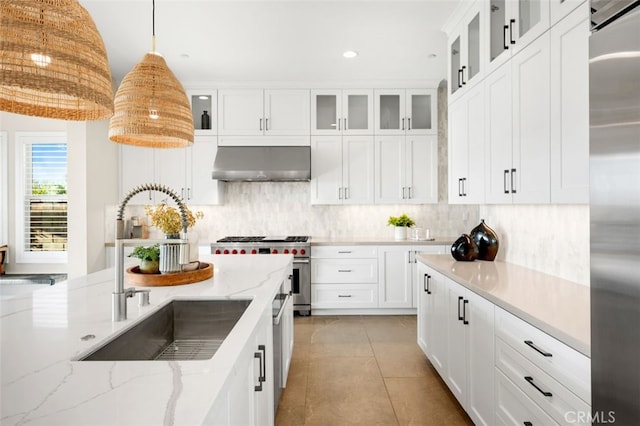 kitchen featuring high quality appliances, under cabinet range hood, decorative light fixtures, a sink, and tasteful backsplash