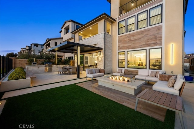 back of house with stone siding, an outdoor living space with a fire pit, exterior kitchen, and fence