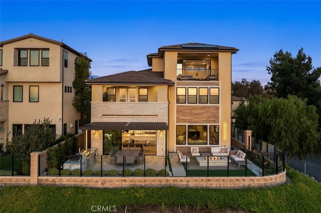 back of property at dusk featuring a balcony, stucco siding, a patio area, roof mounted solar panels, and an outdoor hangout area