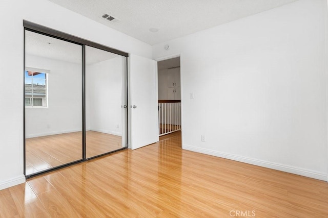 unfurnished bedroom featuring visible vents, baseboards, a textured ceiling, and wood finished floors