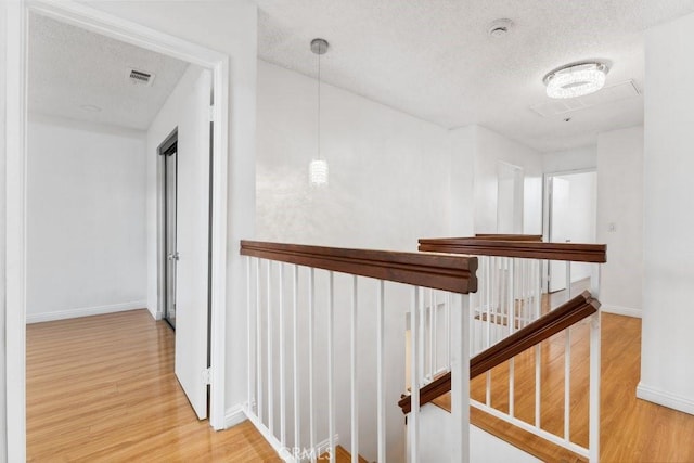 corridor featuring wood finished floors, visible vents, and a textured ceiling