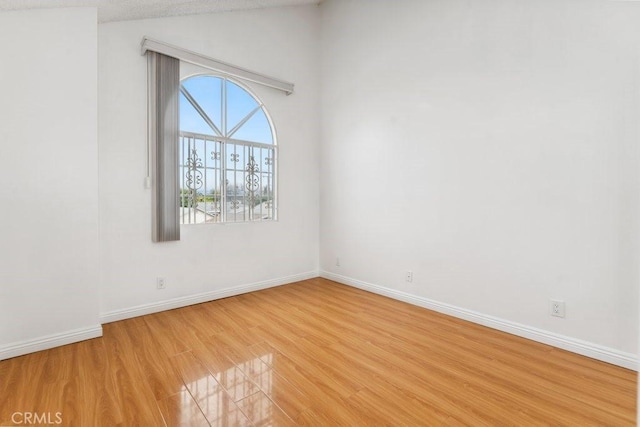 empty room with vaulted ceiling, baseboards, and light wood finished floors