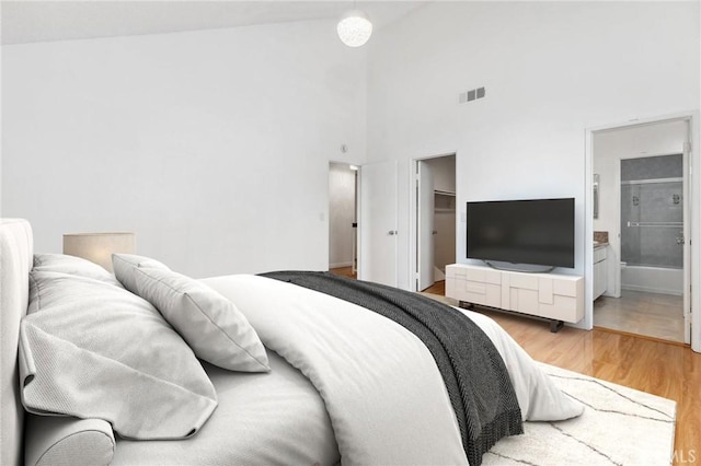 bedroom featuring a spacious closet, visible vents, light wood-type flooring, ensuite bathroom, and a closet