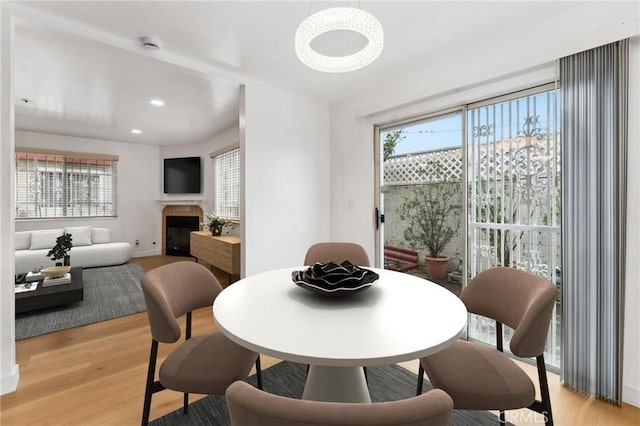 dining space with light wood-type flooring, a tiled fireplace, recessed lighting, an inviting chandelier, and baseboards