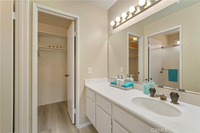 bathroom with a walk in closet, vanity, wood finished floors, and a shower with door